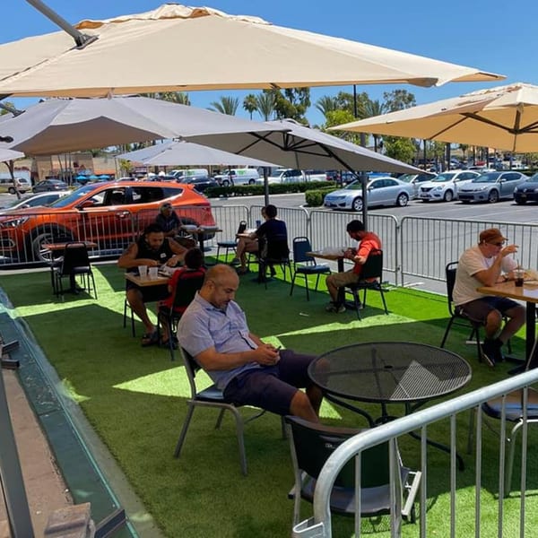 Customers dine outdoors under large umbrellas on artificial turf at Pita's Mediterranean Grill.