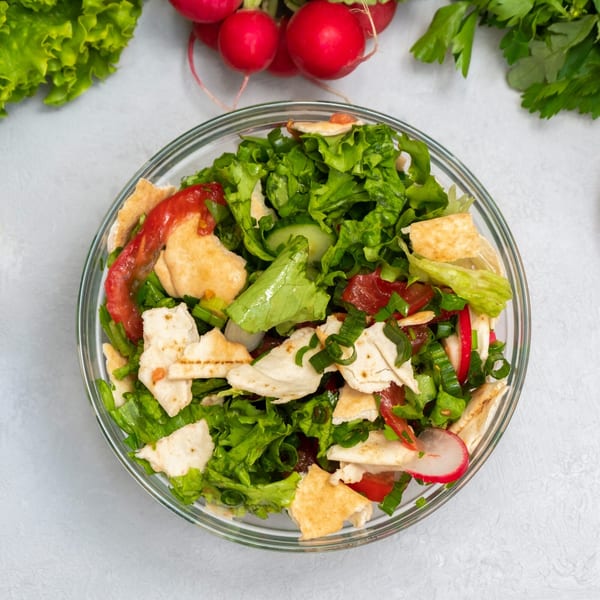 Overhead view of a fresh Mediterranean fattoush salad with pita bread, lettuce, tomatoes, and radishes.