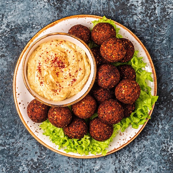 A plate of crispy falafel balls on lettuce with a side of hummus, garnished with paprika.