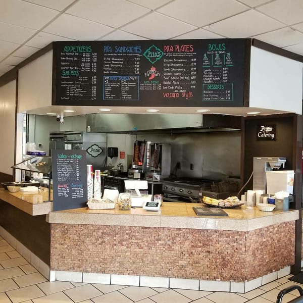 The counter area of Pita's Mediterranean Grill, featuring a large menu board, food preparation equipment, and a serving station.