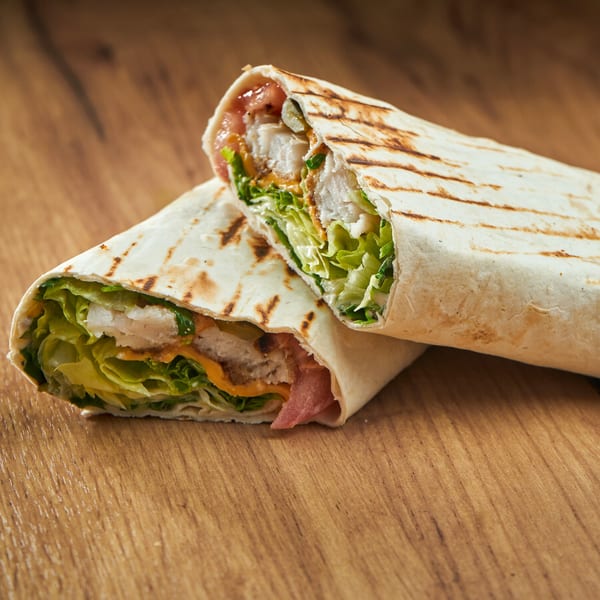 Two halves of a grilled Mediterranean chicken wrap with lettuce, sauce, and pickles on a wooden table.