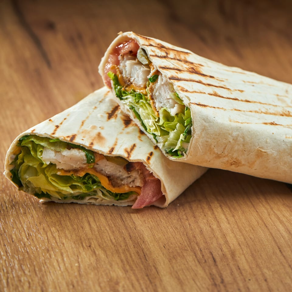 Two halves of a grilled Mediterranean chicken wrap with lettuce, sauce, and pickles on a wooden table.