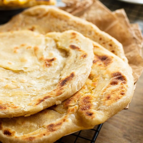 Stack of warm, golden-brown pita bread with slight charring, on a cooling rack.