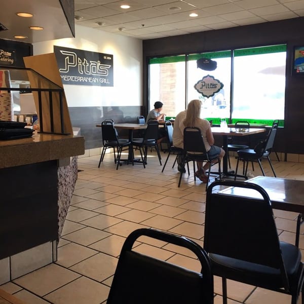 Interior of Pita's Mediterranean Grill with customers seated at tables near large windows.