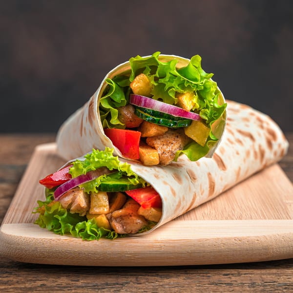 Two Pita's Mediterranean Grill wraps filled with chicken, lettuce, tomatoes, onions, and cucumbers on a wooden board.